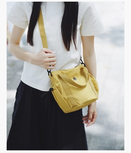 Detail of a bright yellow nylon crossbody bag featuring side drawstrings and metal logo