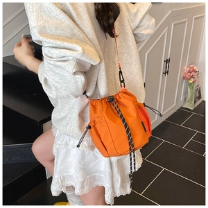 Detail of an orange nylon bucket bag with mesh side pocket and striped drawstrings