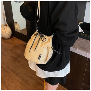 Detail of khaki canvas bucket bag with drawstring closure and side mesh pocket worn by model