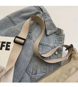 Détail de la bandoulière en nylon et sac bandoulière beige sur fond de veste en jean