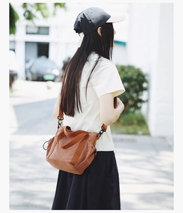 Brown nylon crossbody bag with wide adjustable shoulder strap worn by person outdoors