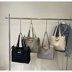 Dettaglio di grandi borse tote in nylon in quattro colori appese a un rack di metallo