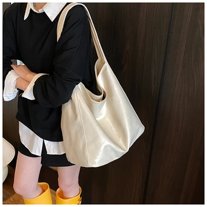 Detail of a large creamy white tote bag in glossy PU leather worn by a model