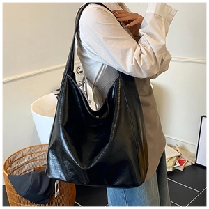 Detail of black glossy leather tote bag with pleated texture and wide shoulder strap