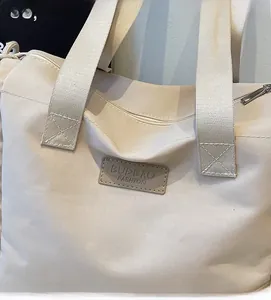 Dettaglio della borsa in tela beige con tracolle larghe e logo in pelle cucito