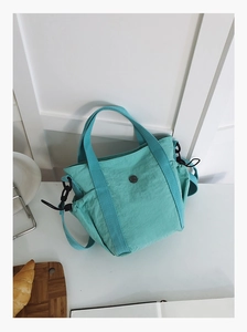 Detail of mint green nylon tote bag featuring drawstring side pocket and round metal logo