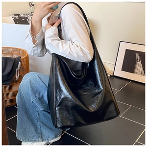 Detail of a large black glossy faux leather tote bag worn as a shoulder bag