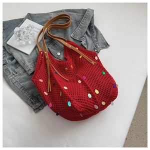 Detail of red crochet tote bag with colorful sequins and brown leather strap on denim
