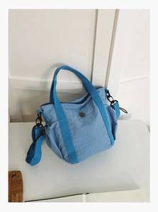 Detail of light blue nylon handbag showing metal logo and adjustable strap attachment