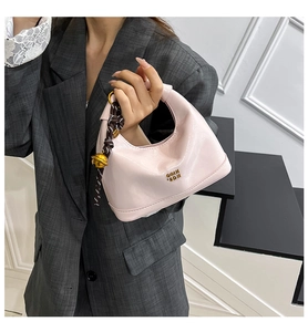 Dettaglio borsa in pelle verniciata rosa chiaro con ciondolo intrecciato e campanella