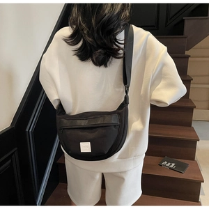 Gros plan d'un sac bandoulière demi-lune en nylon noir imperméable sur l'épaule