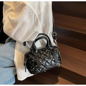 Quilted black Boston bag with silver studs worn by model on a wooden staircase