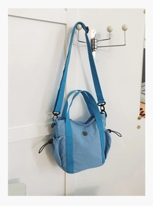 Detail of light blue nylon handbag showing drawstring side pockets and blue webbing handles