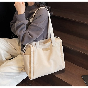 Dettaglio della tasca laterale con coulisse e logo in pelle sulla borsa tote crema
