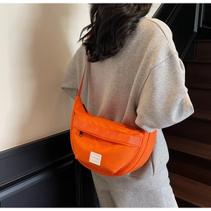 Détail d'un sac bandoulière orange vif en nylon avec étiquette blanche de marque vue de dos