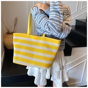 Sac cabas à rayures jaunes et blanches avec lanières en cuir porté par un mannequin chic