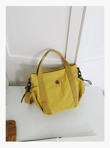 Detail of yellow nylon tote bag with drawstring sides and circular metal logo plaque