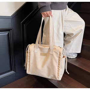 Dettaglio della borsa tote beige con eleganti coulisse laterali e targhetta in pelle