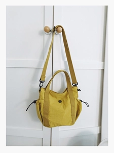 Detail of mustard yellow fabric tote bag with drawstring sides and round black logo