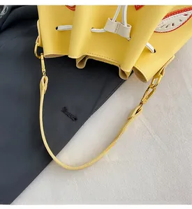 Detail of yellow matte PU leather bucket bag featuring a white drawstring and red embroidery