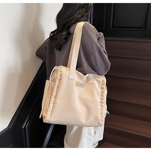 Dettaglio della borsa tote in tela beige con coulisse laterale e inserto in pelle logo