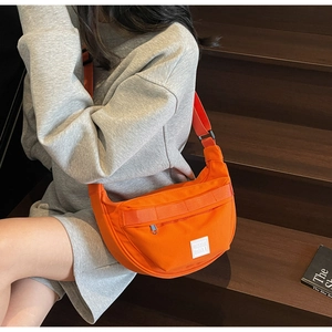 Détail d'un sac bandoulière demi-lune orange en toile porté sur une tenue décontractée