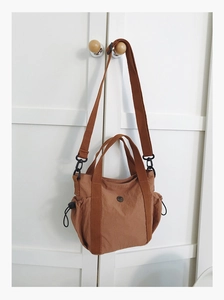 Close-up of brown nylon crossbody bag featuring drawstring side pockets and wide strap