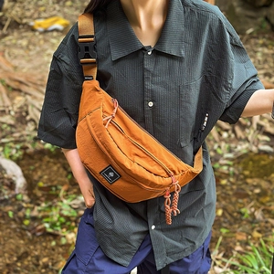 Burnt orange nylon chest bag featuring adjustable strap and woven zipper pullers