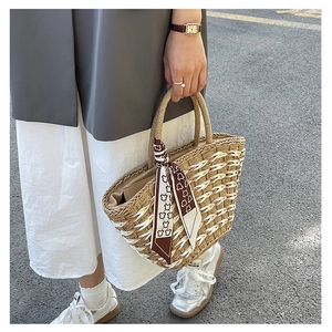 Detail of woven straw handbag featuring a decorative brown bear silk scarf on handle