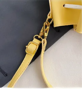 Detail of yellow bucket bag featuring golden metal hardware and adjustable shoulder strap