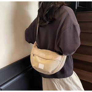 Détail du sac bandoulière beige en demi-lune avec étiquette tissée et large sangle