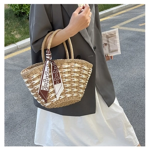 Handcrafted straw handbag with patterned silk scarf shown in a stylish outdoor setting