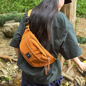 Detail of a bright orange nylon crossbody bag with zipper pulls and textured fabric