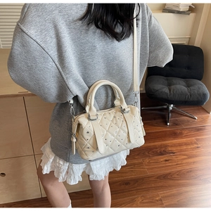 Quilted beige bucket bag with silver studs worn by a model in a minimalist lifestyle setting