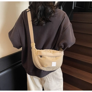 Détail du sac bandoulière demi-lune beige avec large sangle sur une tenue marron