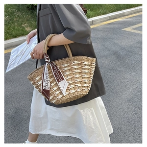 Detail of hand-woven straw tote with bear-patterned silk scarf on a street model