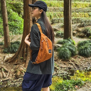 Close-up of burnt orange nylon crescent waist bag with zipper detail in outdoor setting