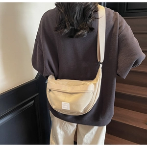 Détail du sac bandoulière en demi-lune crème avec sangle tissée porté par un mannequin