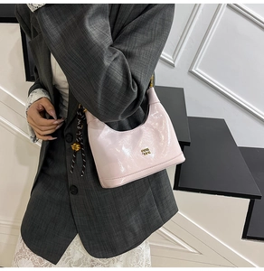 Dettaglio ravvicinato della borsa in pelle verniciata rosa chiaro con logo dorato e tracolla