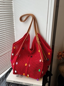 Red knit tote bag with colorful sequins and brown leather straps on a white book