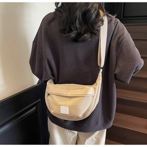 Sac bandoulière en toile beige de forme demi-lune avec sangle large sur modèle