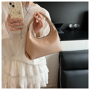Detail of beige lychee texture leather hobo bag held by model in modern office setting