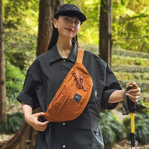 Detail of orange nylon chest bag with woven zipper pull and adjustable black strap