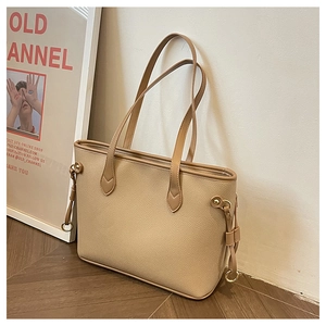 Close-up of beige tote bag showing high-quality lychee texture and round metal charm