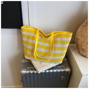 Détail du sac cabas tissé à rayures jaunes et blanches avec lanières en cuir sur valise