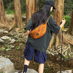 Detail of burnt orange chest bag with braided zipper puller and brand logo patch