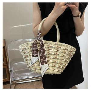 Detail of woven straw tote bag with brown pattern scarf accent on the handle