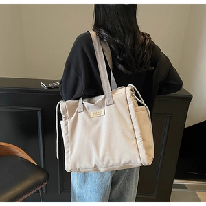 Dettaglio della borsa tote in tela beige con coulisse laterale e logo in pelle sulla borsa