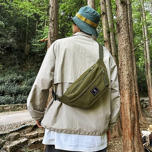 Detail of army green nylon chest bag worn outdoors with woven zipper pull and logo label