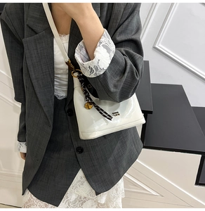 Dettaglio della borsa in pelle verniciata bianca con logo in metallo e ciondolo a righe